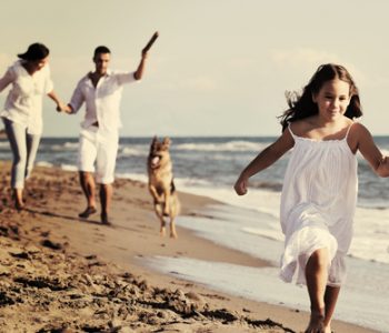 happy-family-playing-with-dog-on-beach-PL9XNMW